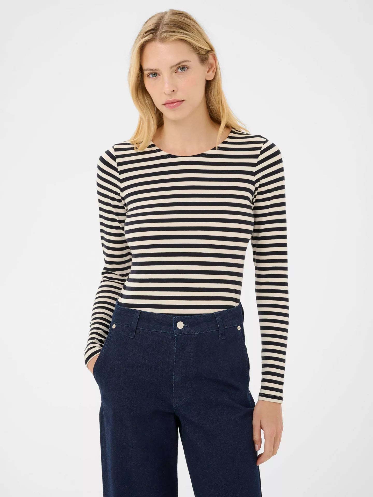 Woman wearing a Navy striped long-sleeve top with blue pants on a white background