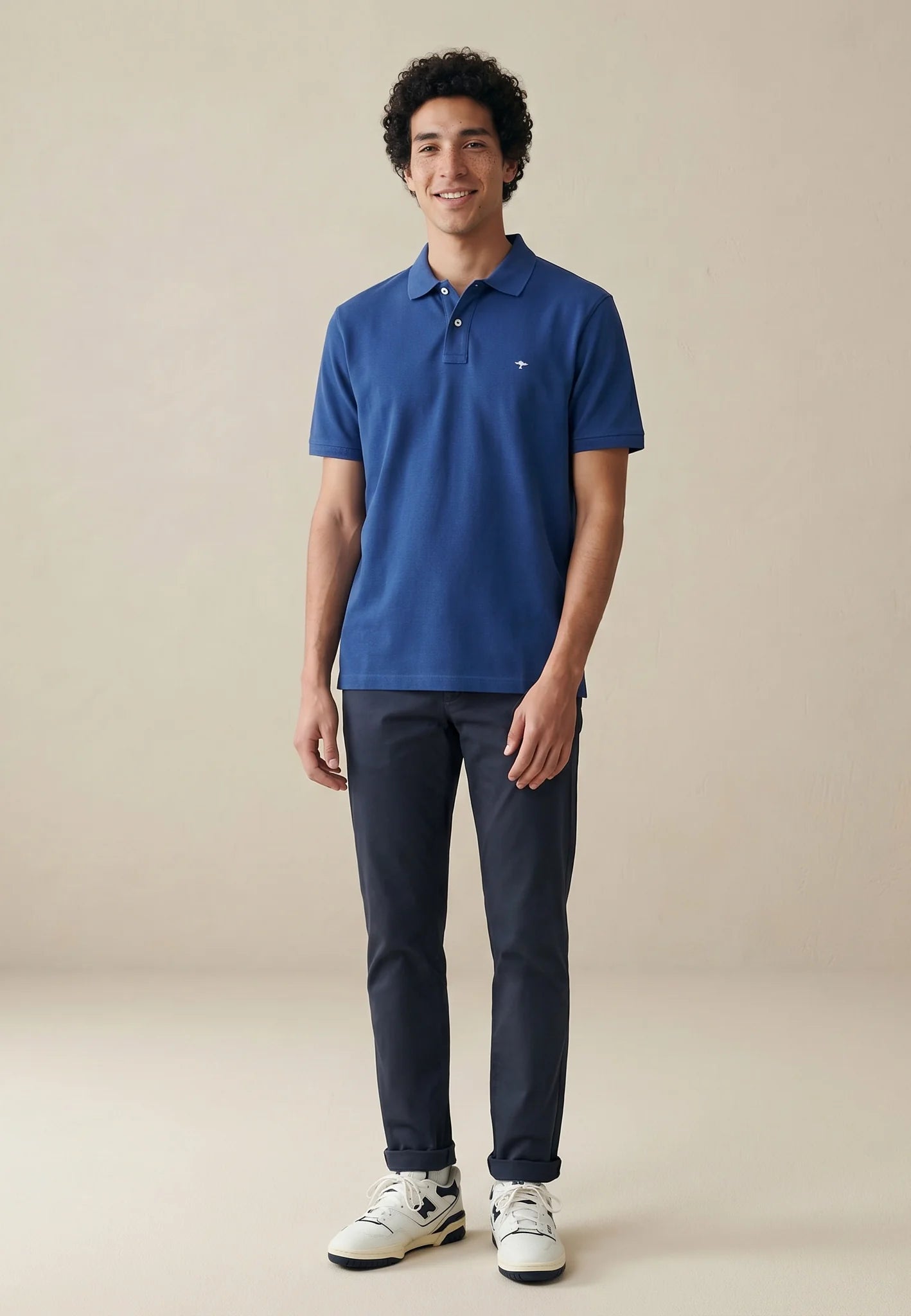 Man wearing a blue polo shirt and dark pants on a beige background