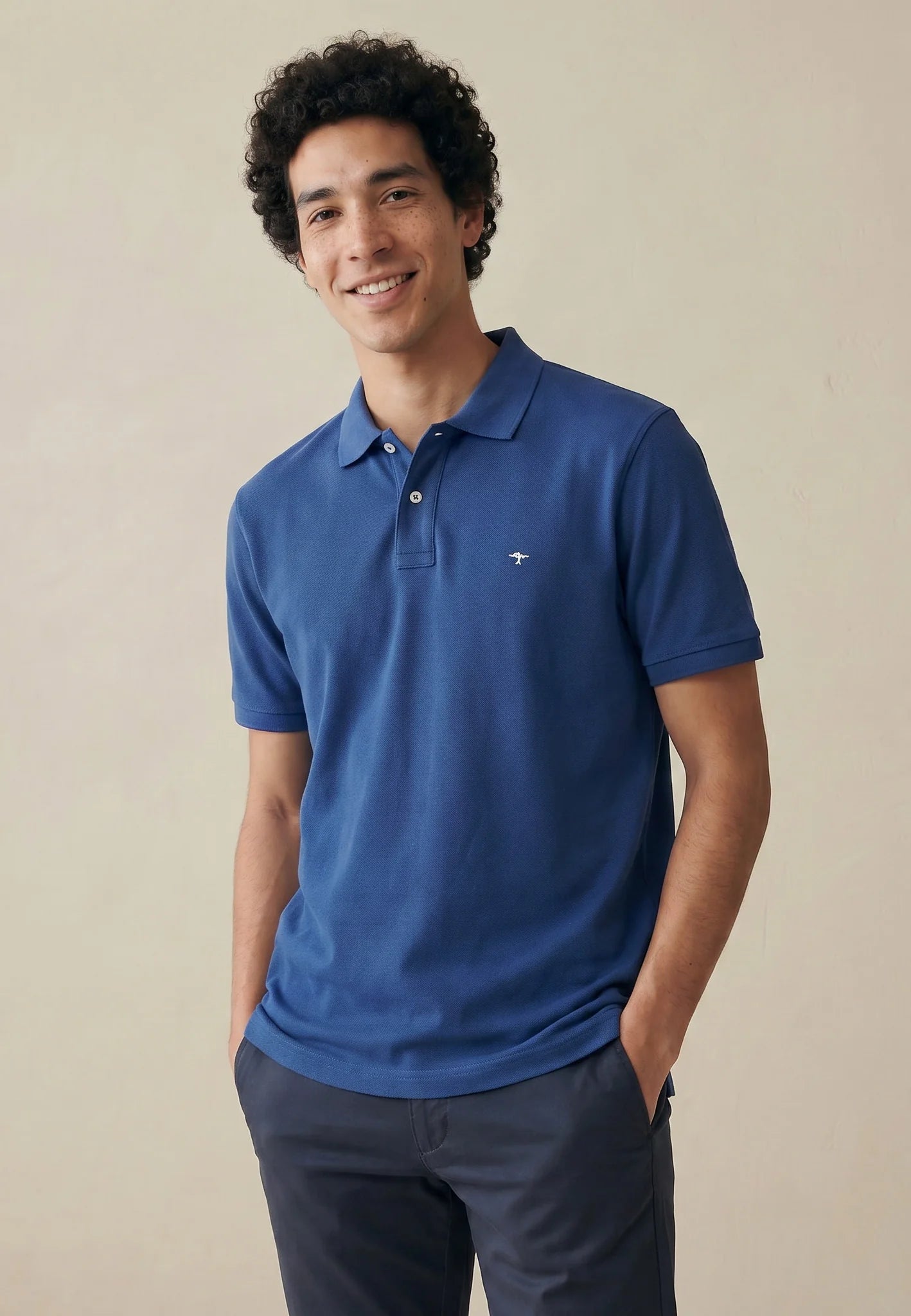 Man wearing a blue polo shirt with a logo on a beige background