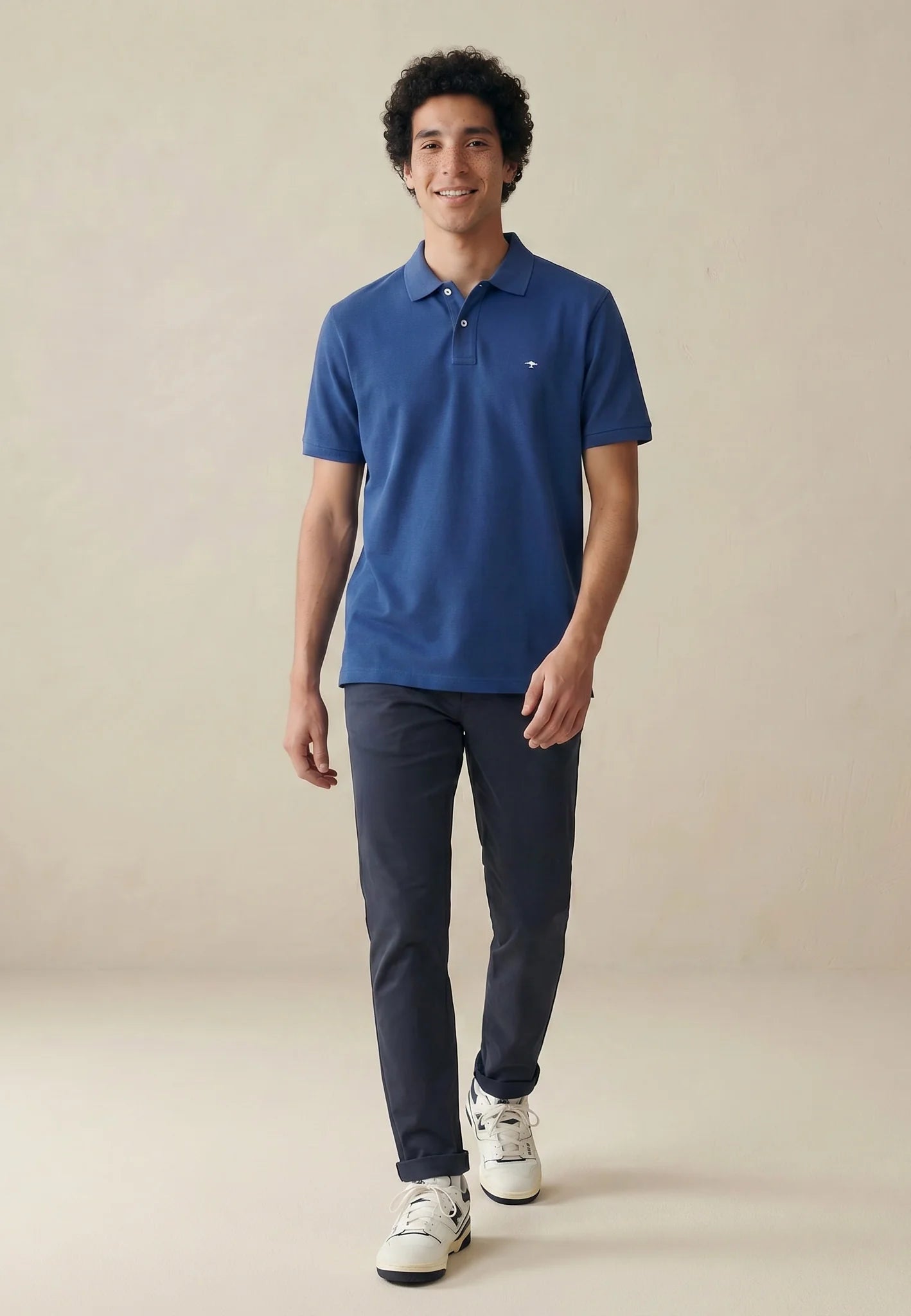 Man wearing a blue polo shirt and navy pants on a beige background
