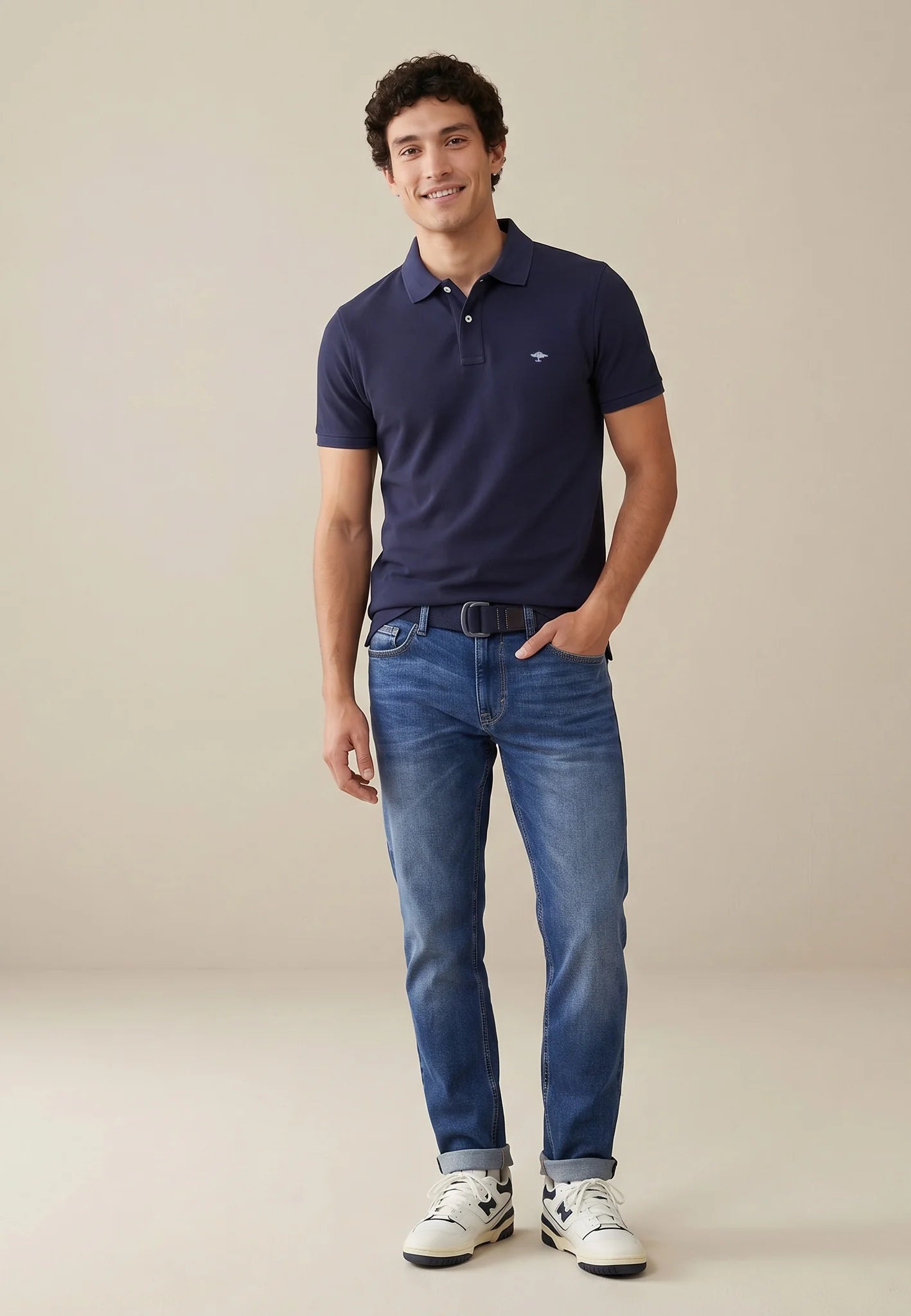 Man wearing a navy polo shirt and blue jeans against a beige background