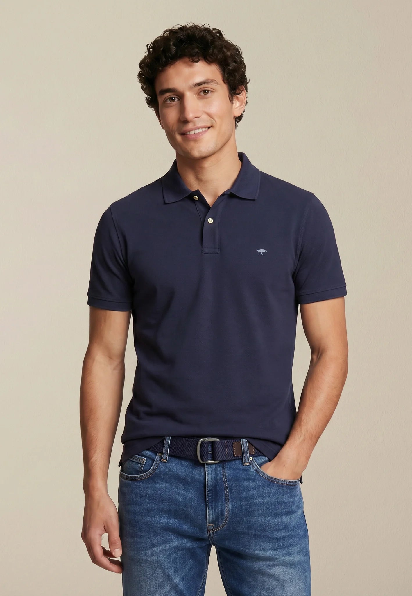 Man wearing a navy polo shirt and blue jeans against a beige background