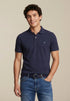 Man wearing a navy polo shirt and blue jeans against a beige background