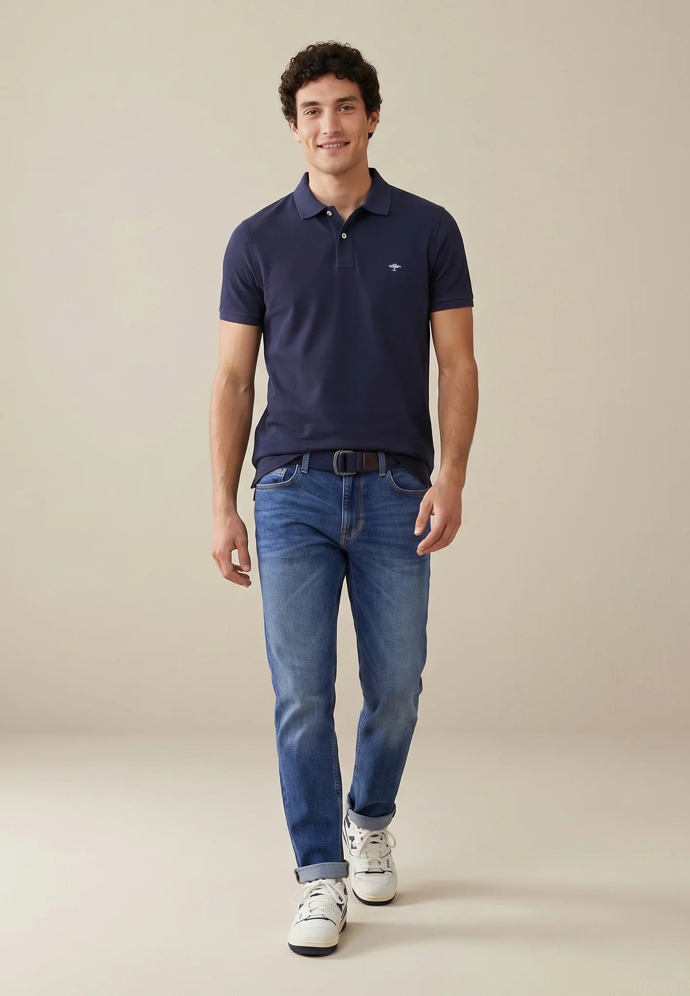 Man wearing a navy polo shirt and blue jeans on a beige background