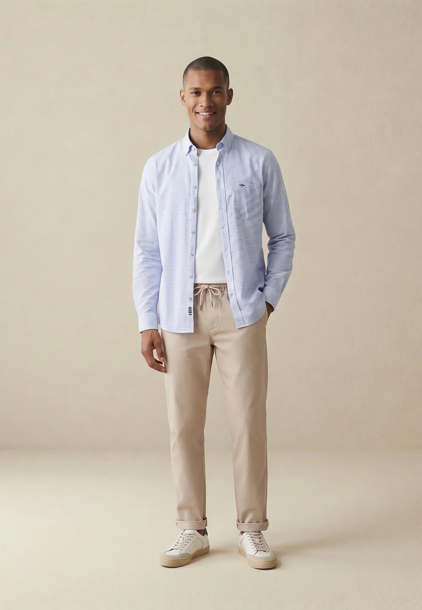Man wearing a light blue shirt, beige pants, and white sneakers on a beige background