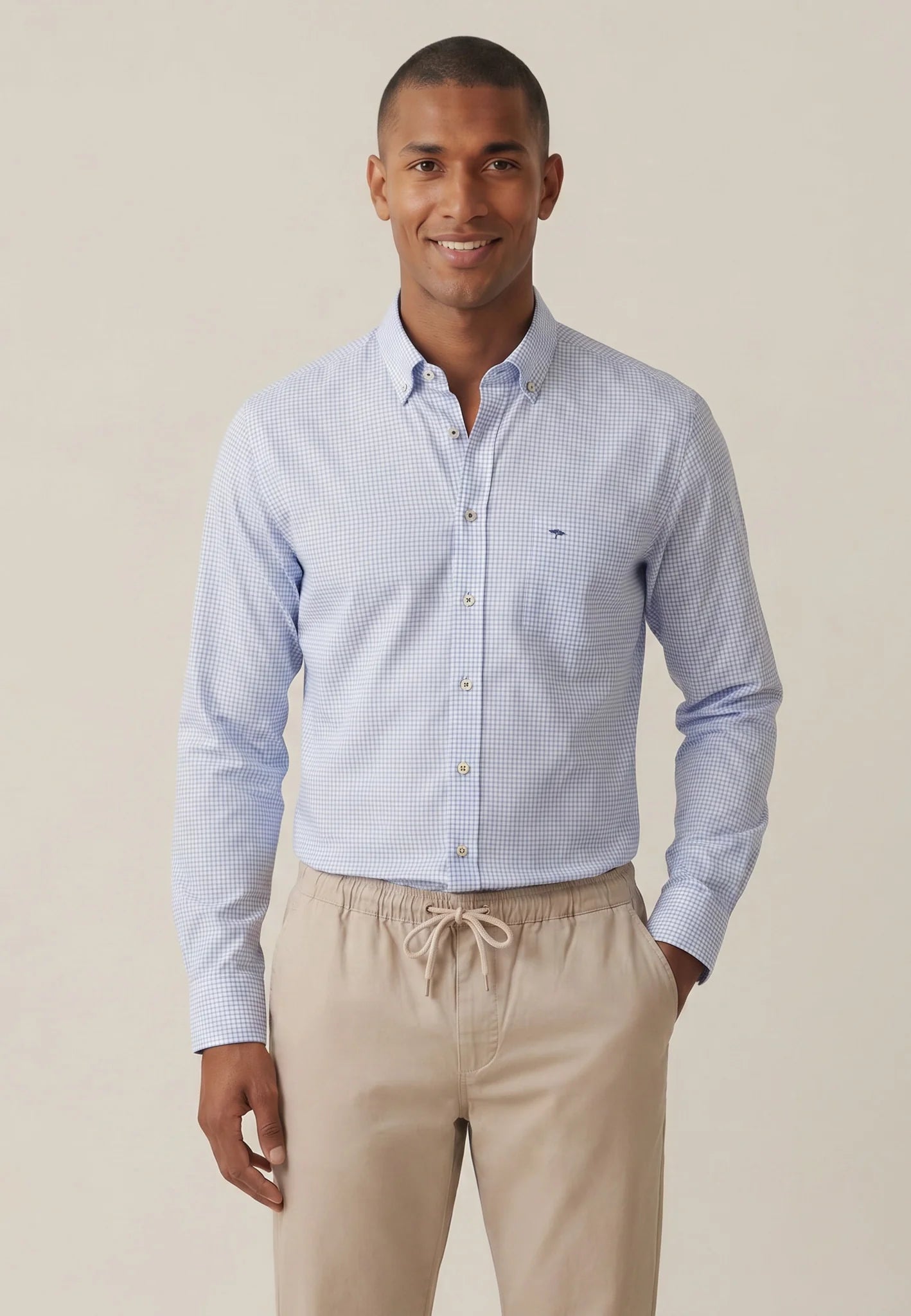 Man wearing a light blue checkered shirt and beige pants against a beige background