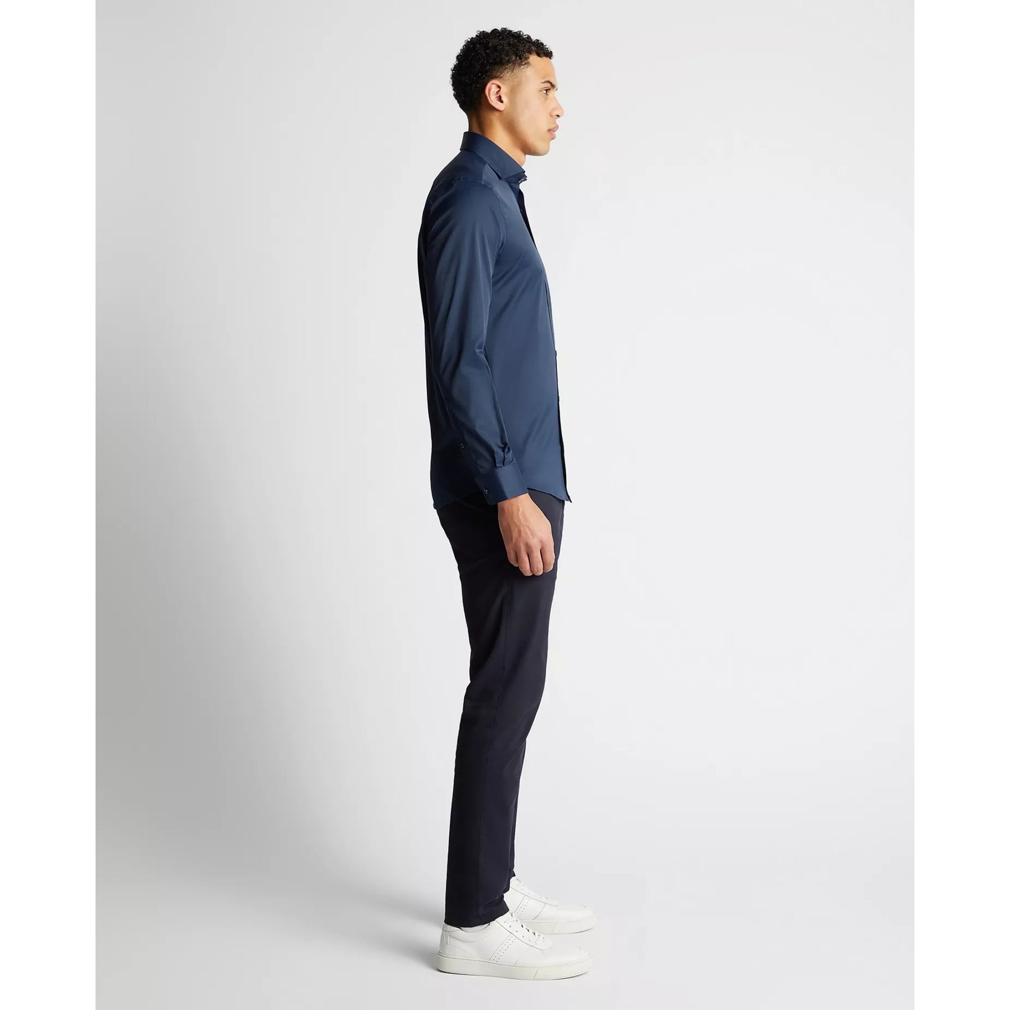 Man wearing a blue shirt and dark pants on a white background