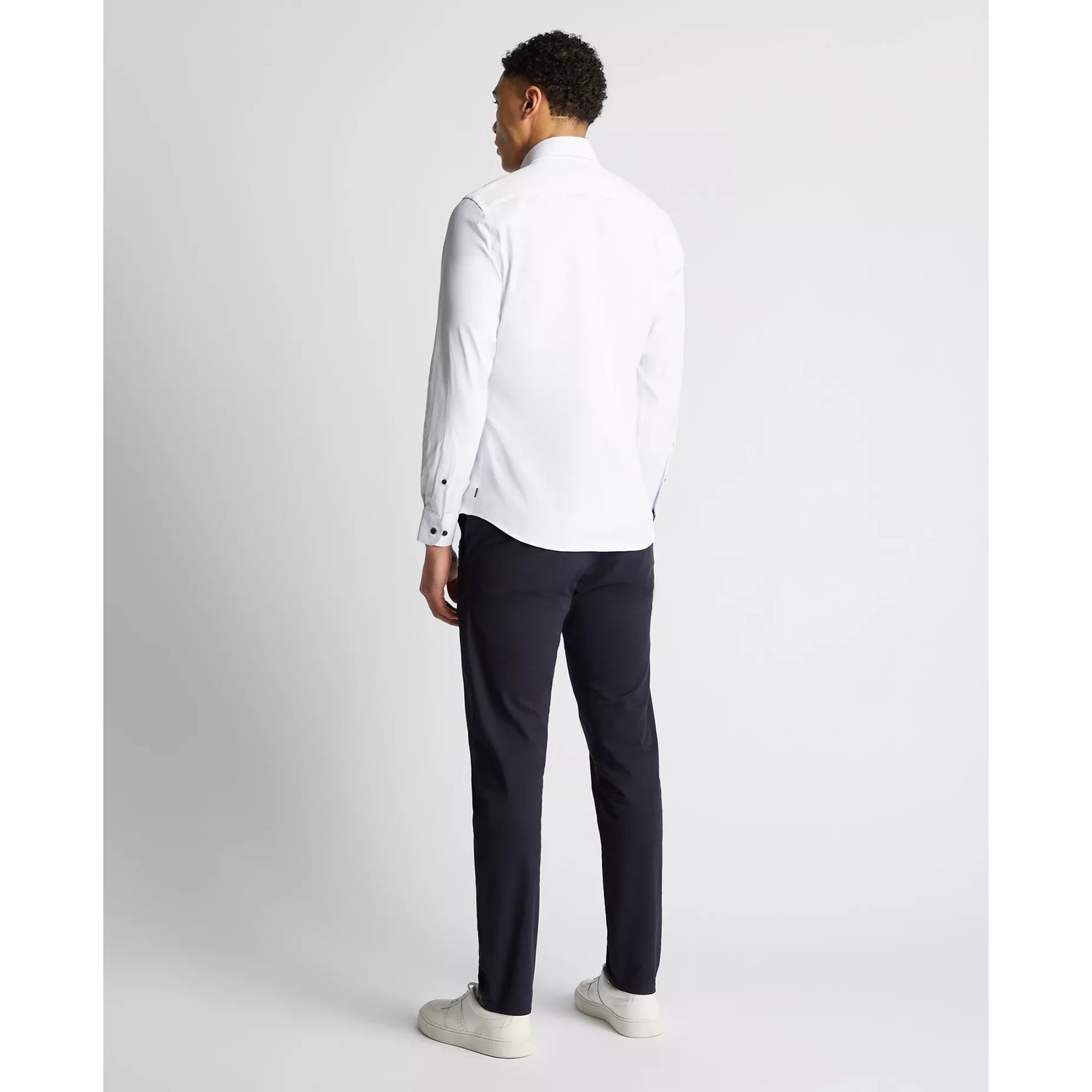 Man wearing a white shirt and dark pants on a light gray background