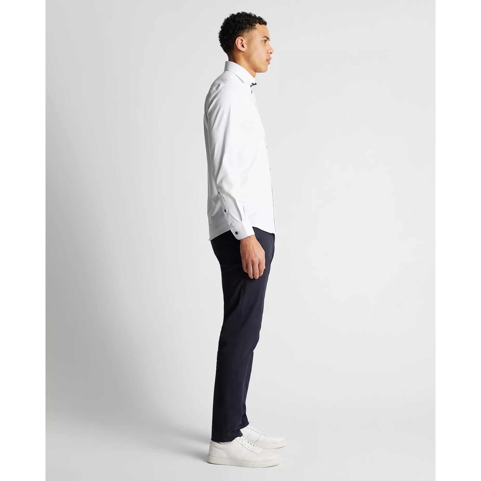 Man wearing a white dress shirt and dark pants on a light gray background