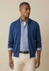 Man wearing a blue cardigan over a striped shirt with beige pants on a beige background