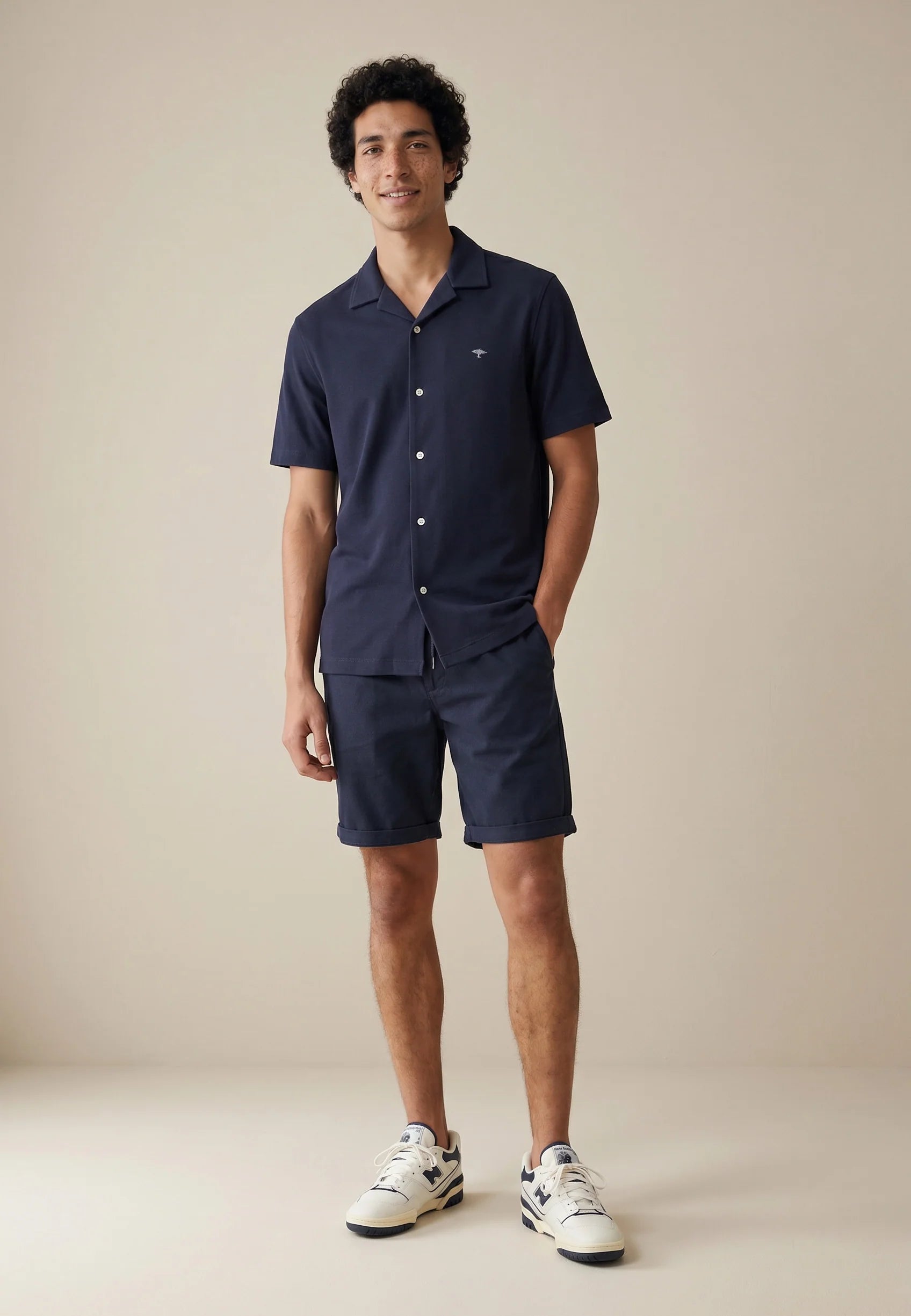 Man wearing a navy blue shirt and shorts set on a beige background