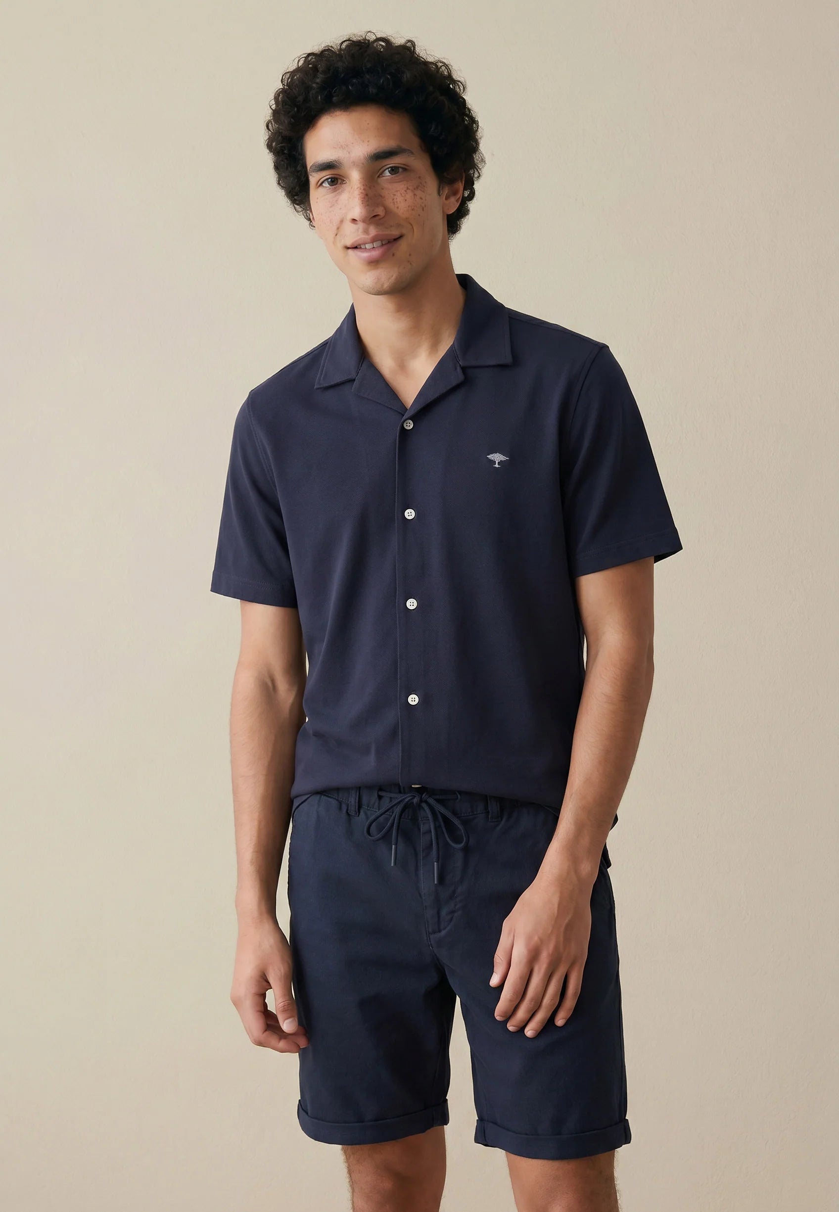 Man wearing a navy blue shirt and shorts set against a beige background
