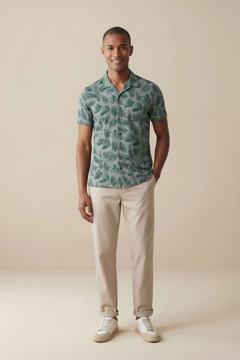 Man wearing a patterned Cuban shirt and beige pants against a beige background