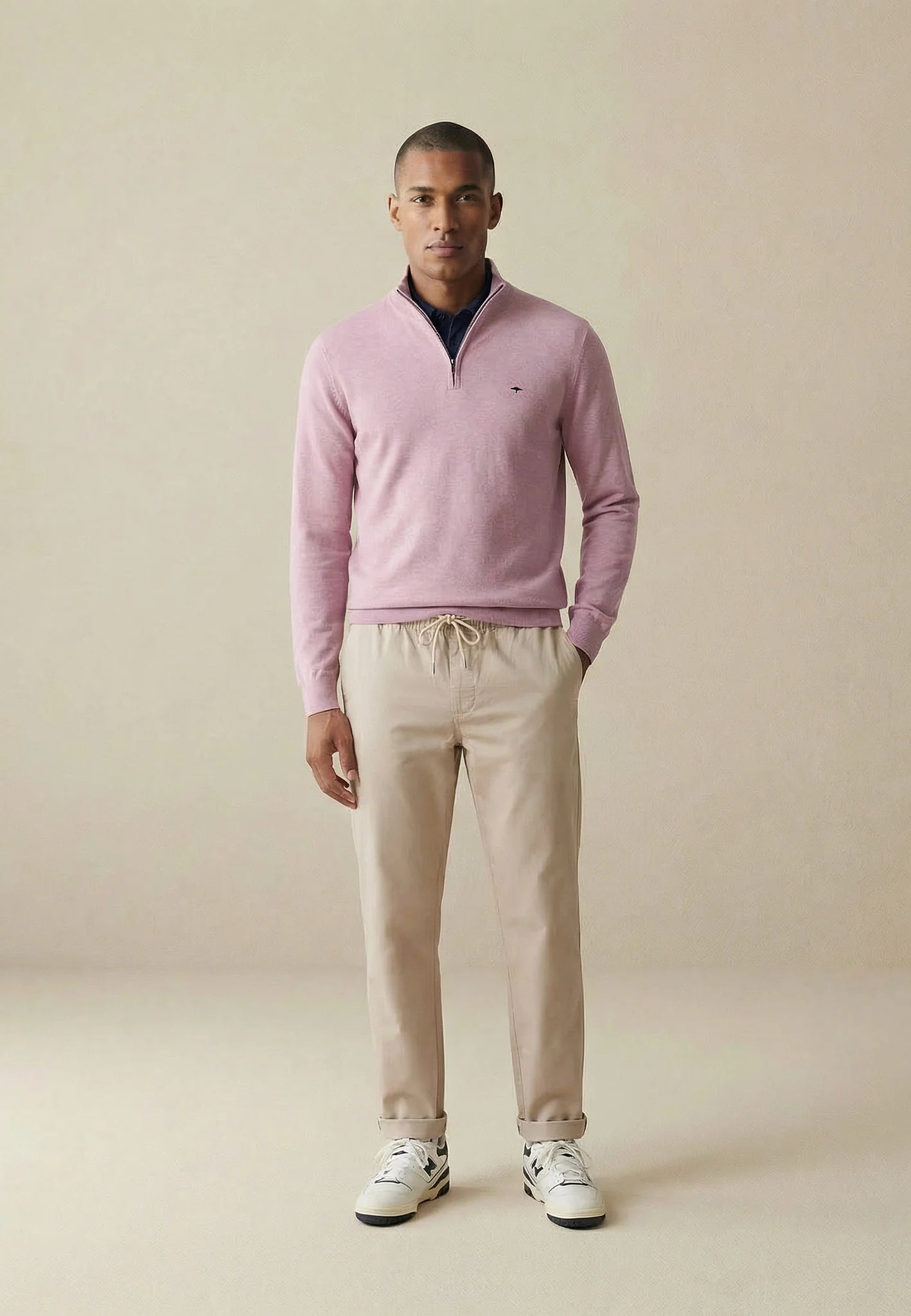 Man wearing a pink sweater and beige pants on a beige background