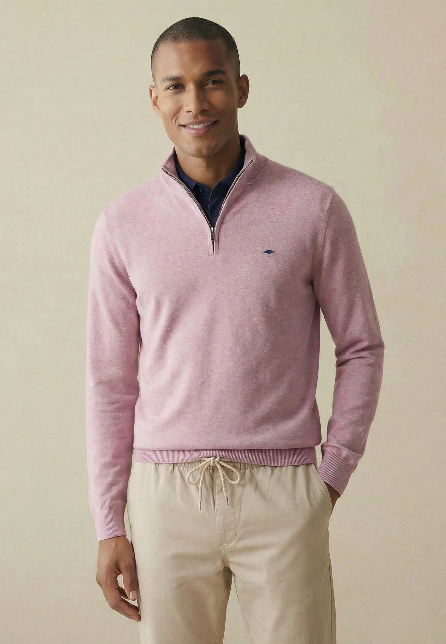 Man wearing a pink half-zip sweater and beige pants against a beige background