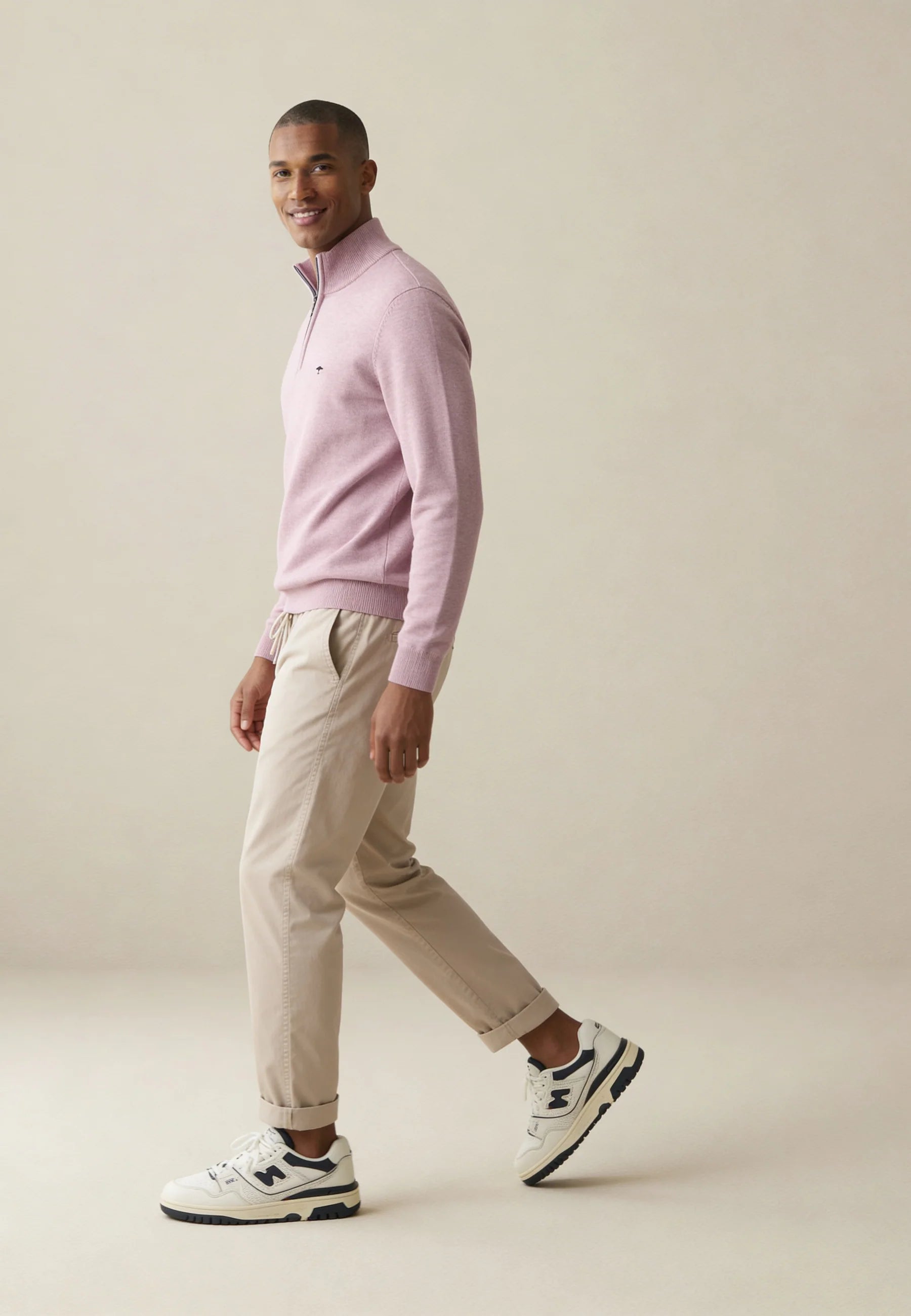 Man wearing a light pink sweater and beige pants on a plain background