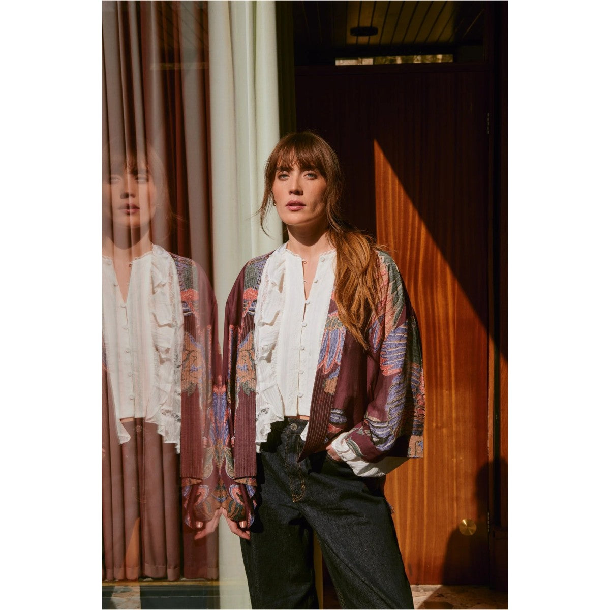 Woman wearing a patterned shirt with a blurred reflection in the mirror.