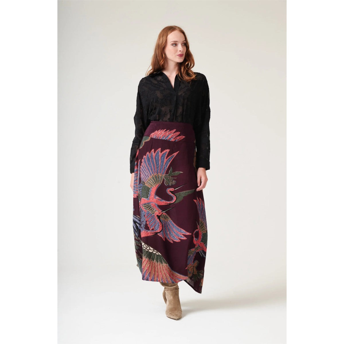 Woman wearing a black shirt and a long, patterned skirt on a white background