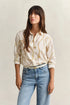 Woman wearing a patterned blouse and jeans against a plain background