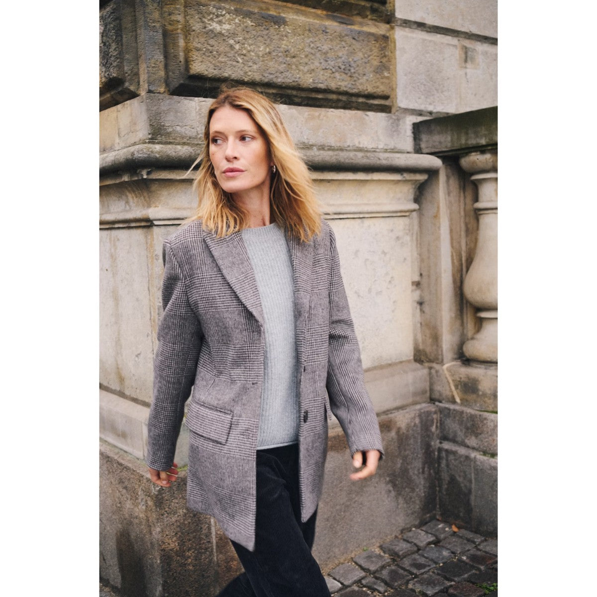Woman wearing a gray coat standing against a stone wall.
