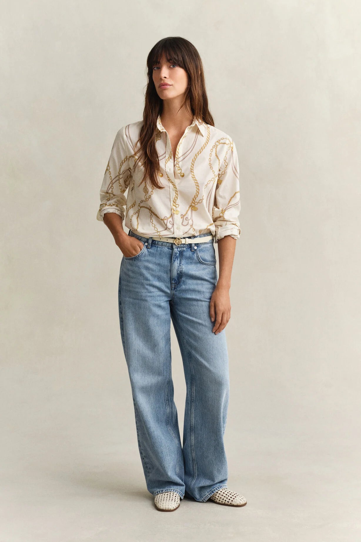 Woman wearing a patterned blouse and blue jeans on a plain background