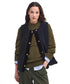 A model wearing a dark navy blue textured cardigan vest over an olive green ribbed sweater, styled with green trousers and a light blue shirt, against a plain white background.