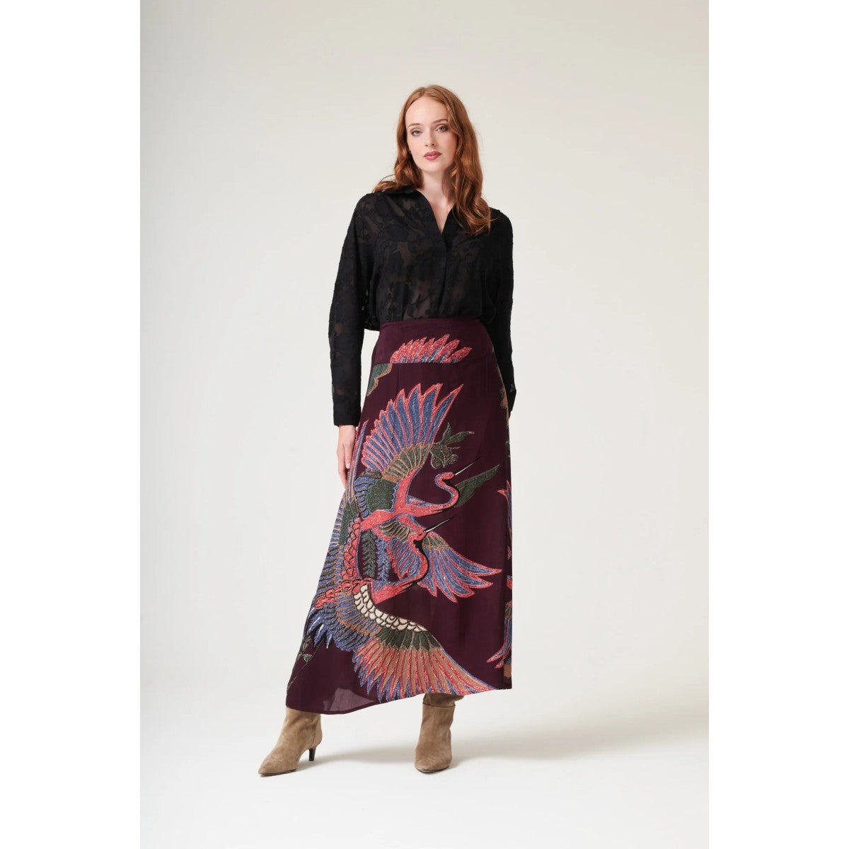 Woman wearing a black top and a long, patterned skirt with a white background