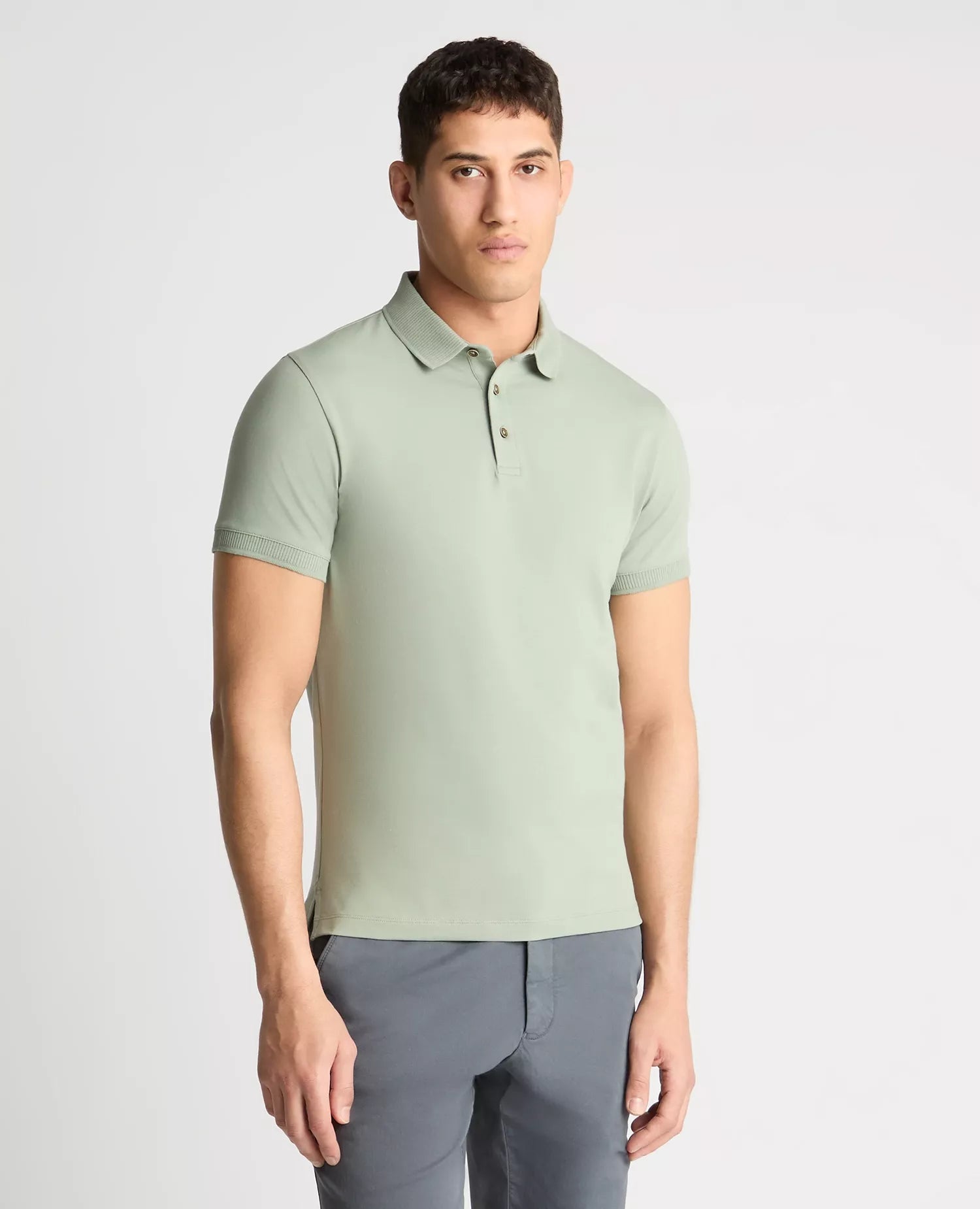 Man wearing a light green polo shirt and gray pants on a white background