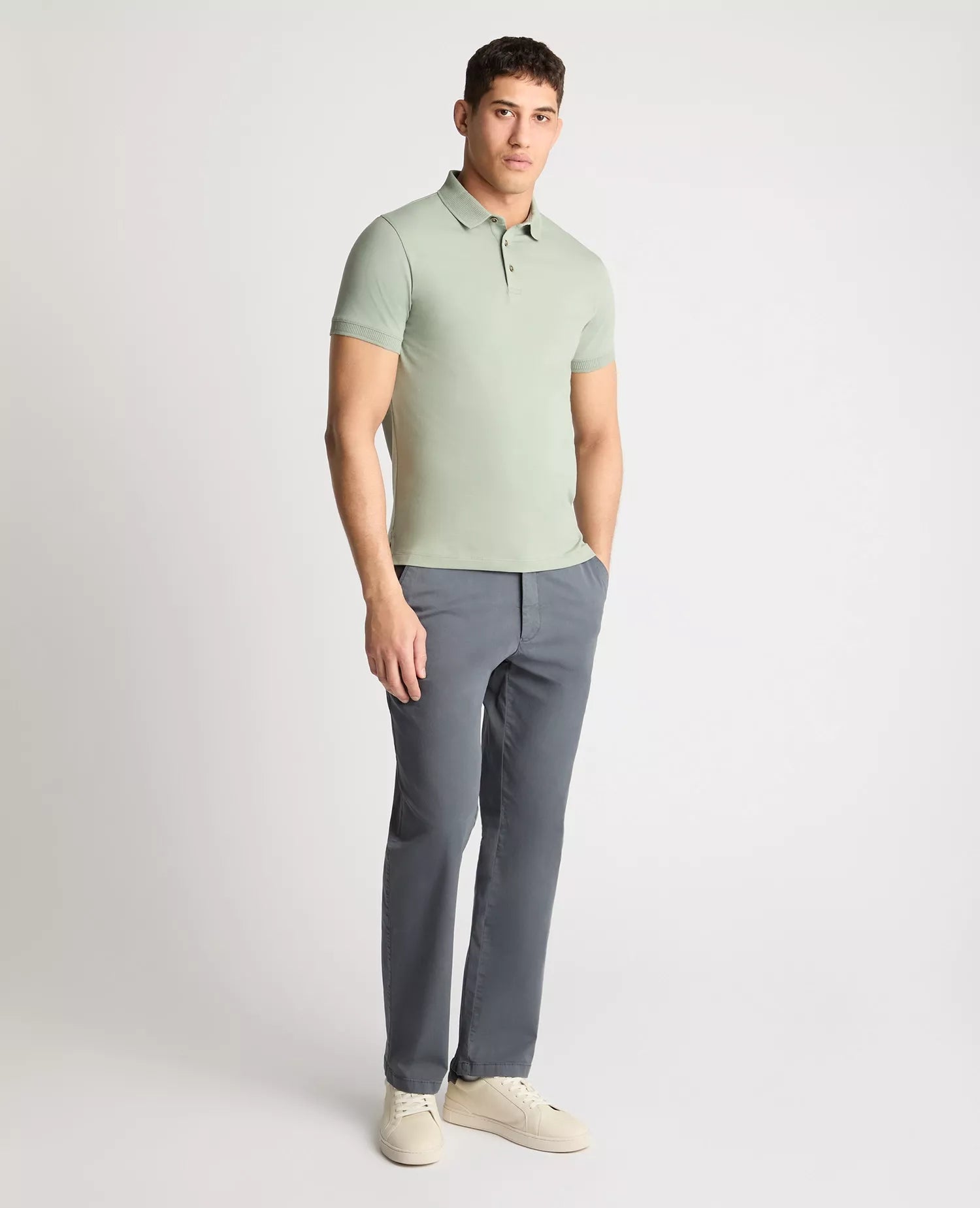 Man wearing a light green polo shirt and gray pants on a white background