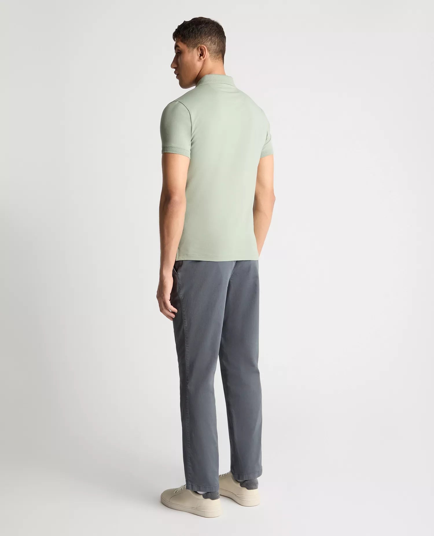 Man wearing a light green polo shirt and gray pants on a white background