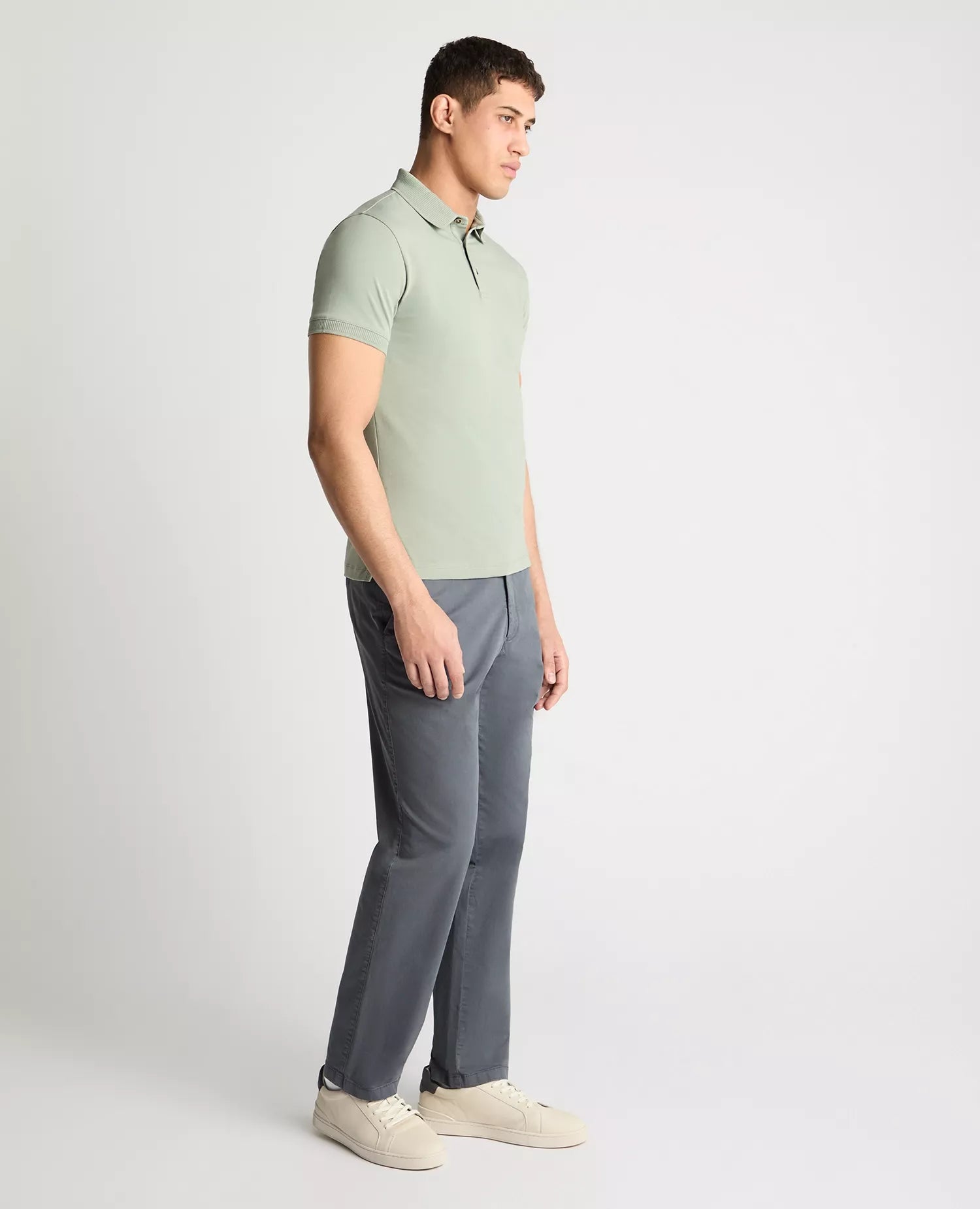 Man wearing a light green polo shirt and gray pants on a white background