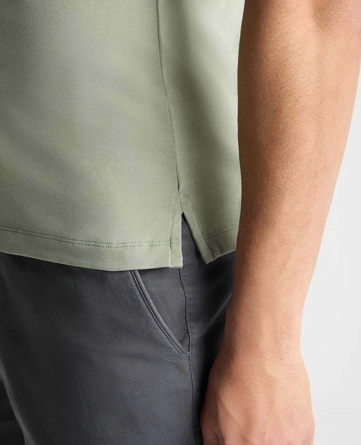 Close-up of a person wearing a green shirt and dark pants on a light gray background