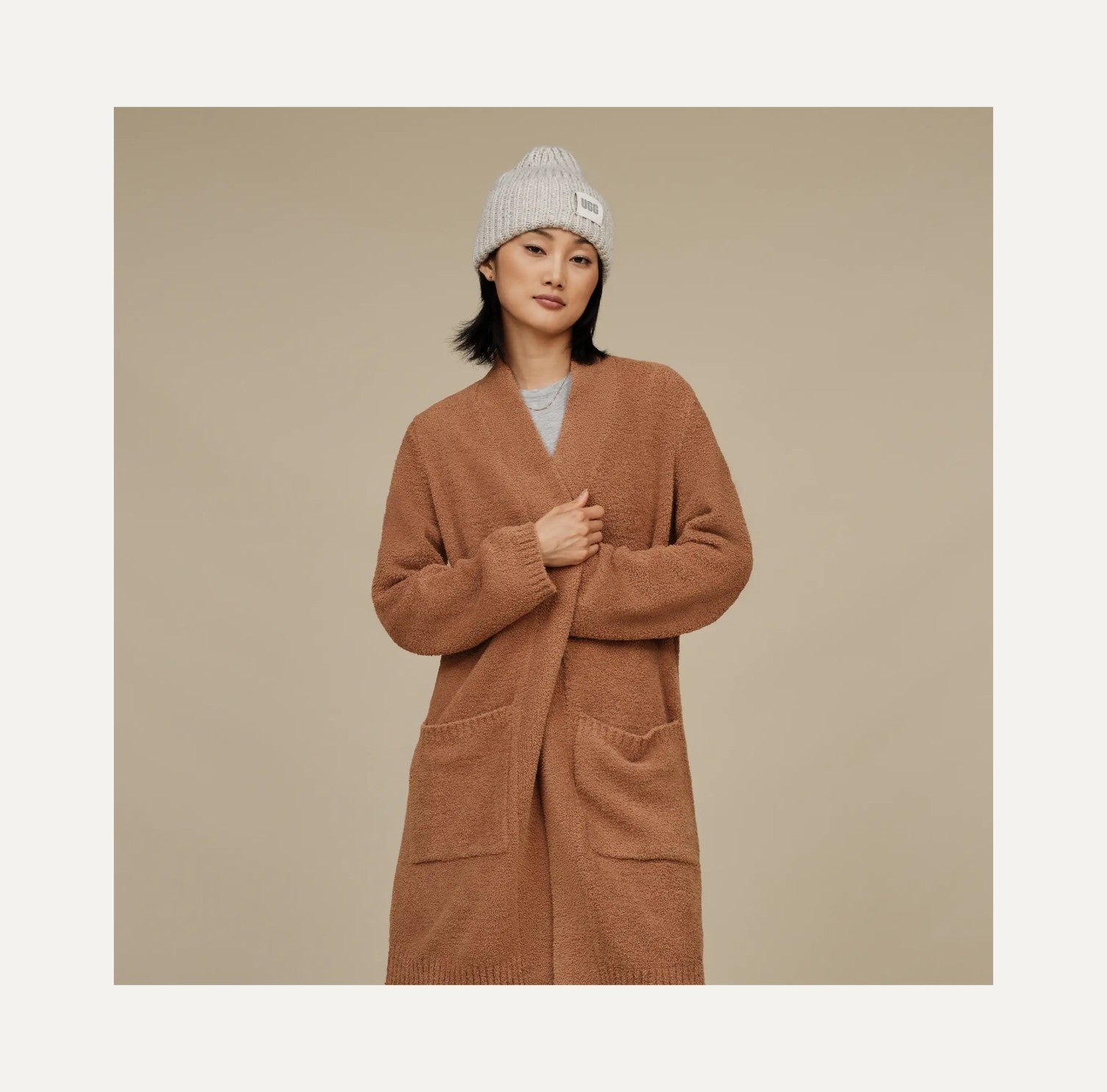 Woman wearing a brown cardigan and gray beanie against a beige background