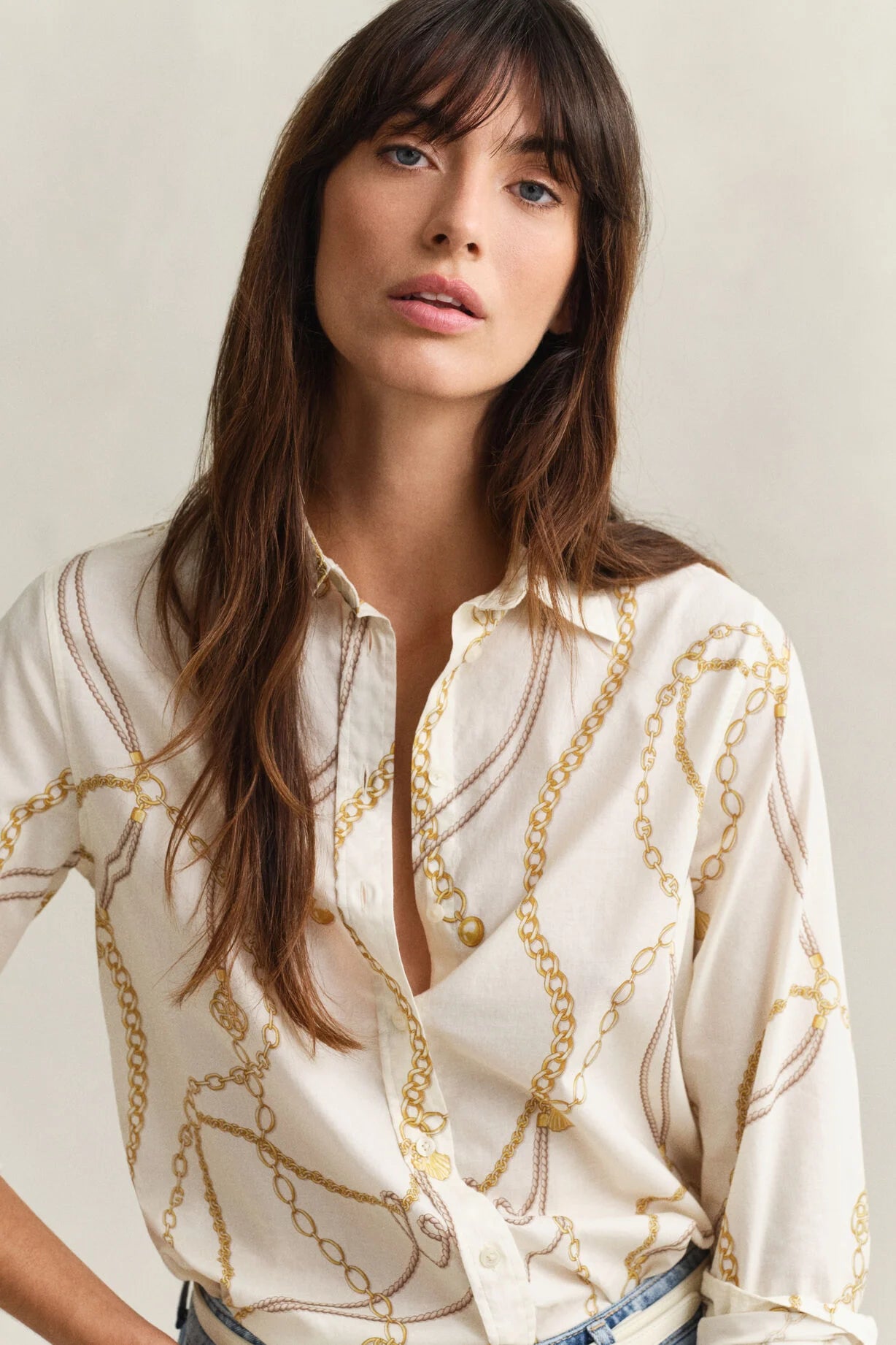 Woman wearing a cream-colored blouse with gold chain pattern against a neutral background