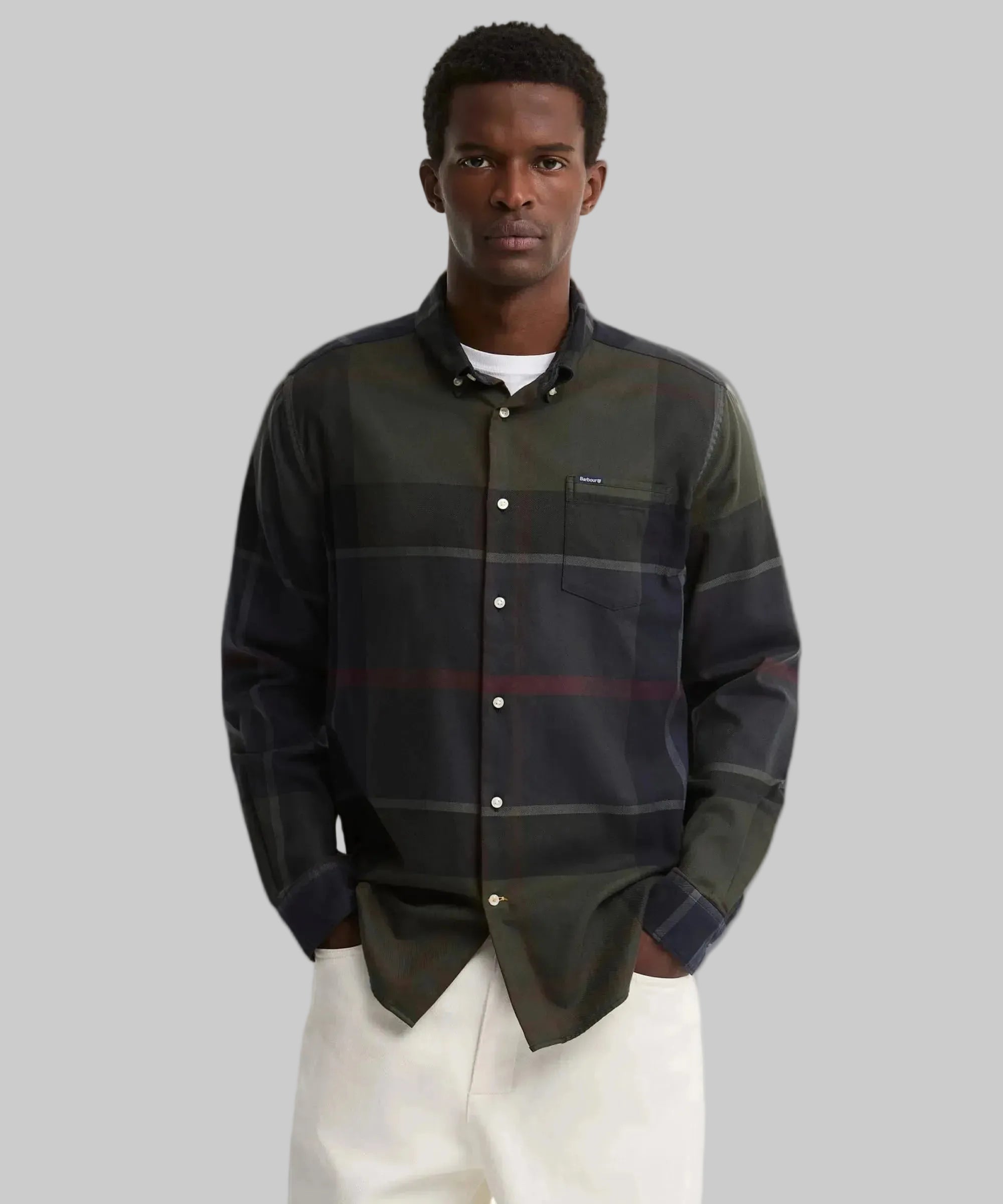 A man wearing a Barbour dark green and navy plaid button-down shirt with a chest pocket, paired with white pants, against a plain white background.