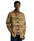 A man wearing a Barbour tan and brown plaid button-down shirt over a navy and cream striped t-shirt, paired with dark blue jeans, photographed against a solid white background.