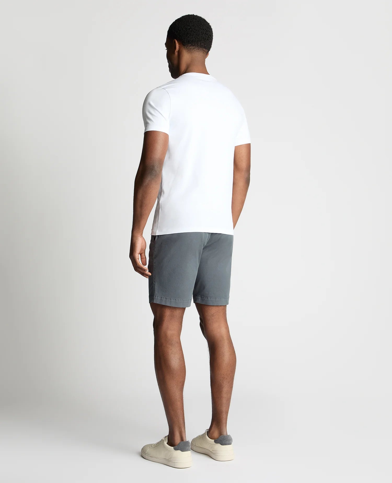 Man wearing a white t-shirt and gray shorts on a light gray background