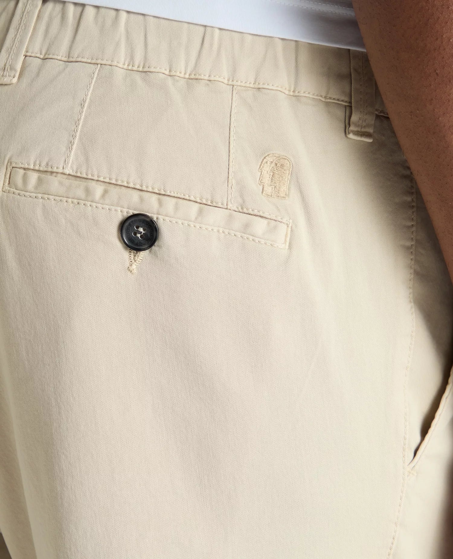 Close-up of beige pants with a button and brand logo.