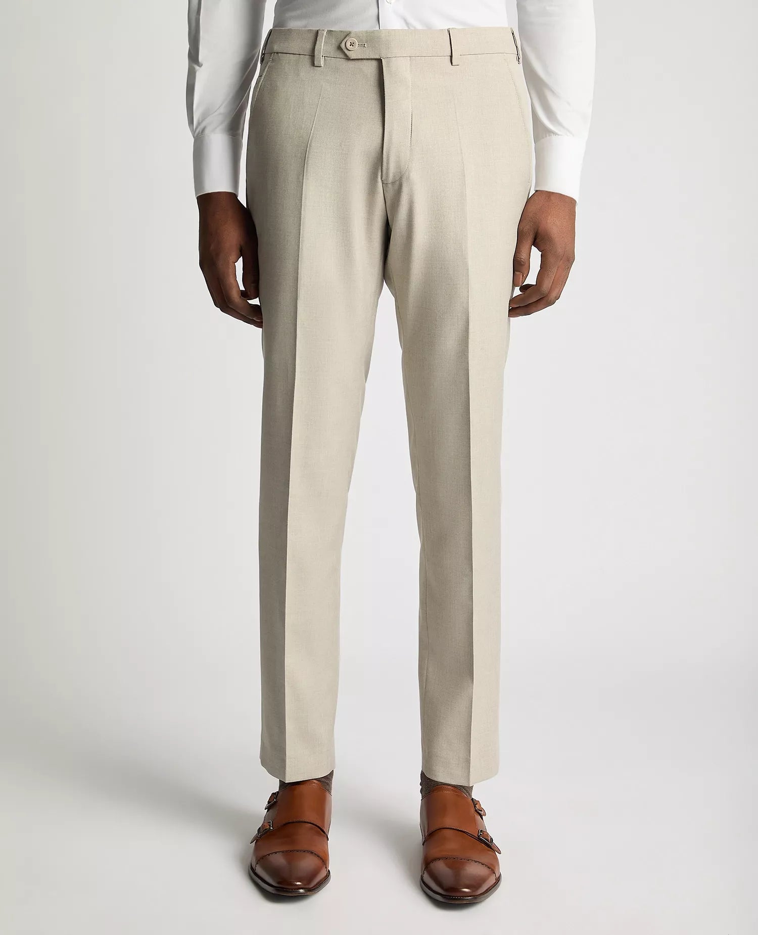 Beige dress pants worn with a white shirt and brown shoes on a light gray background