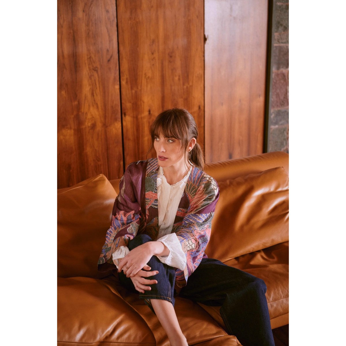 Woman sitting on a brown leather couch in a room with wooden walls.