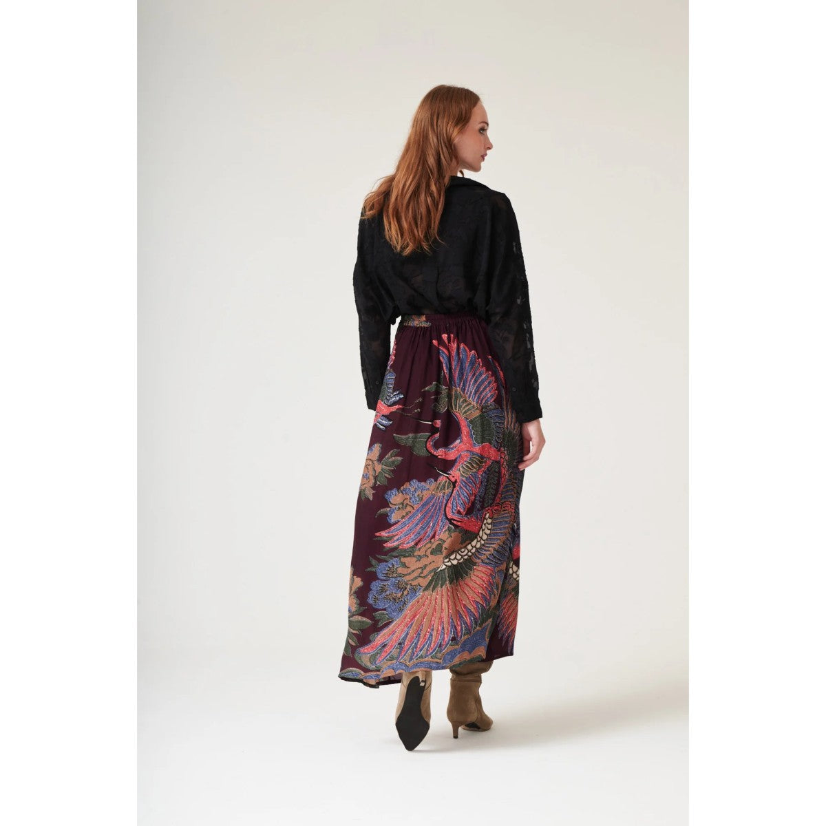 Woman wearing a black top and colorful patterned skirt on a white background