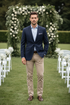 Navy blue wool blazer with two buttons and side vents, featuring a contrast trim on the ticket pocket and a buttonhole detail.