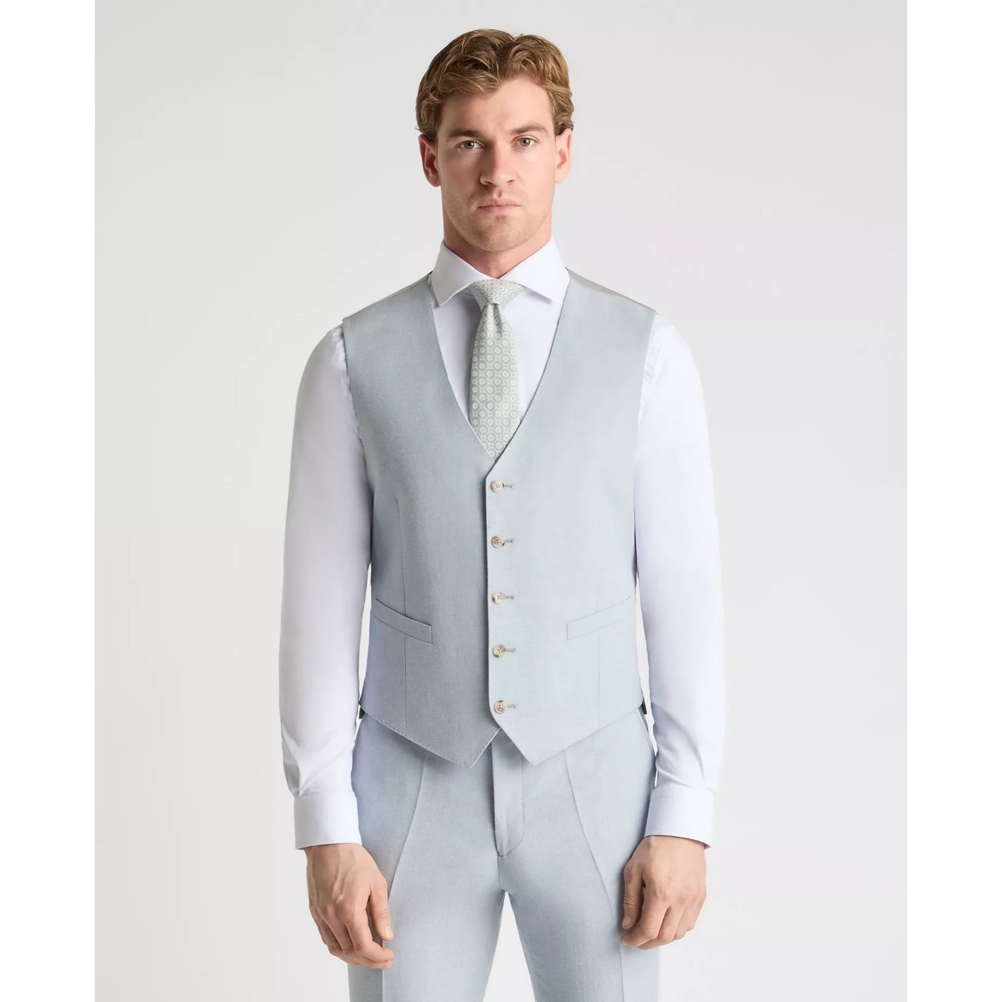 Man wearing a sky blue vest over a white shirt with a light gray tie on a white background