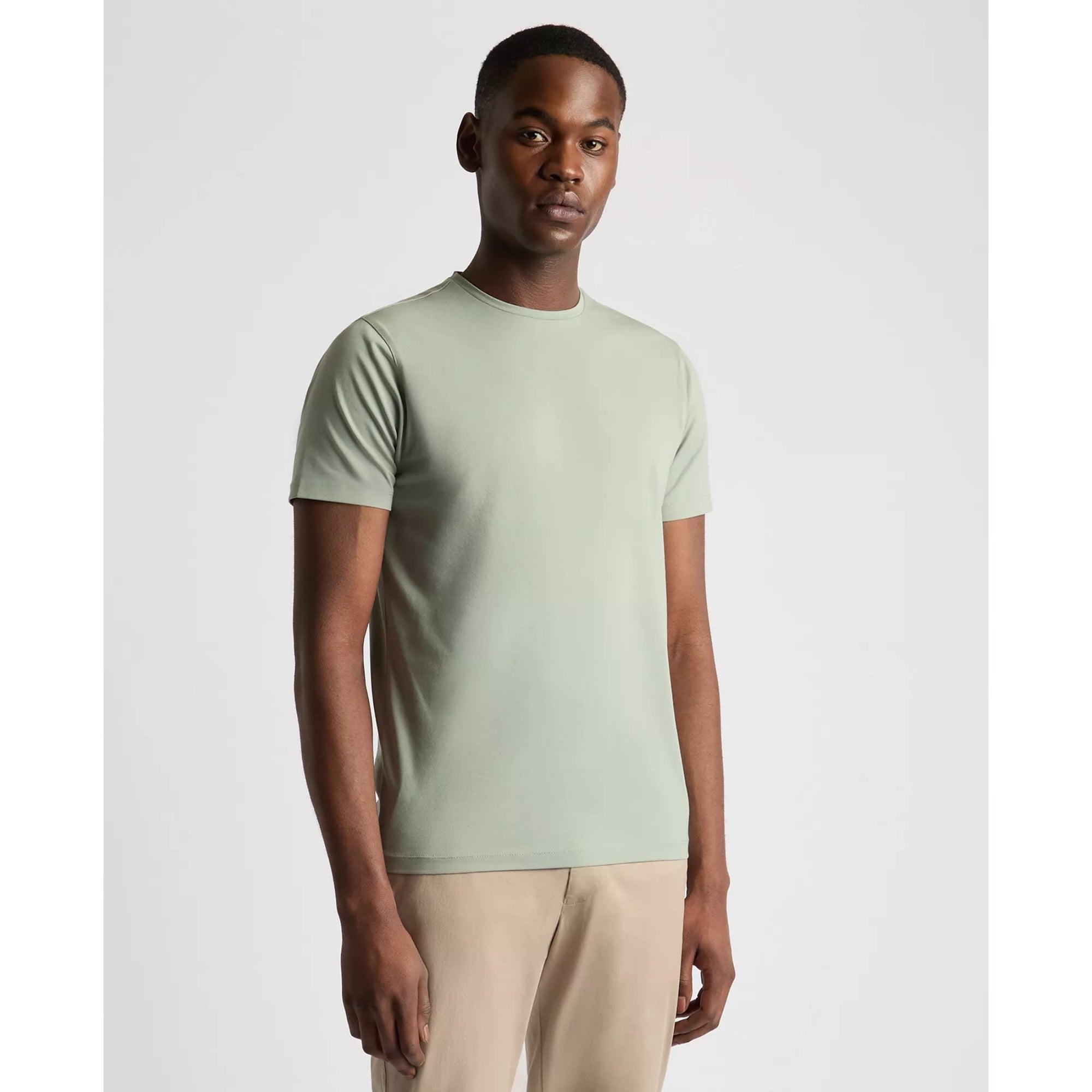 Man wearing a light green t-shirt and beige pants on a white background