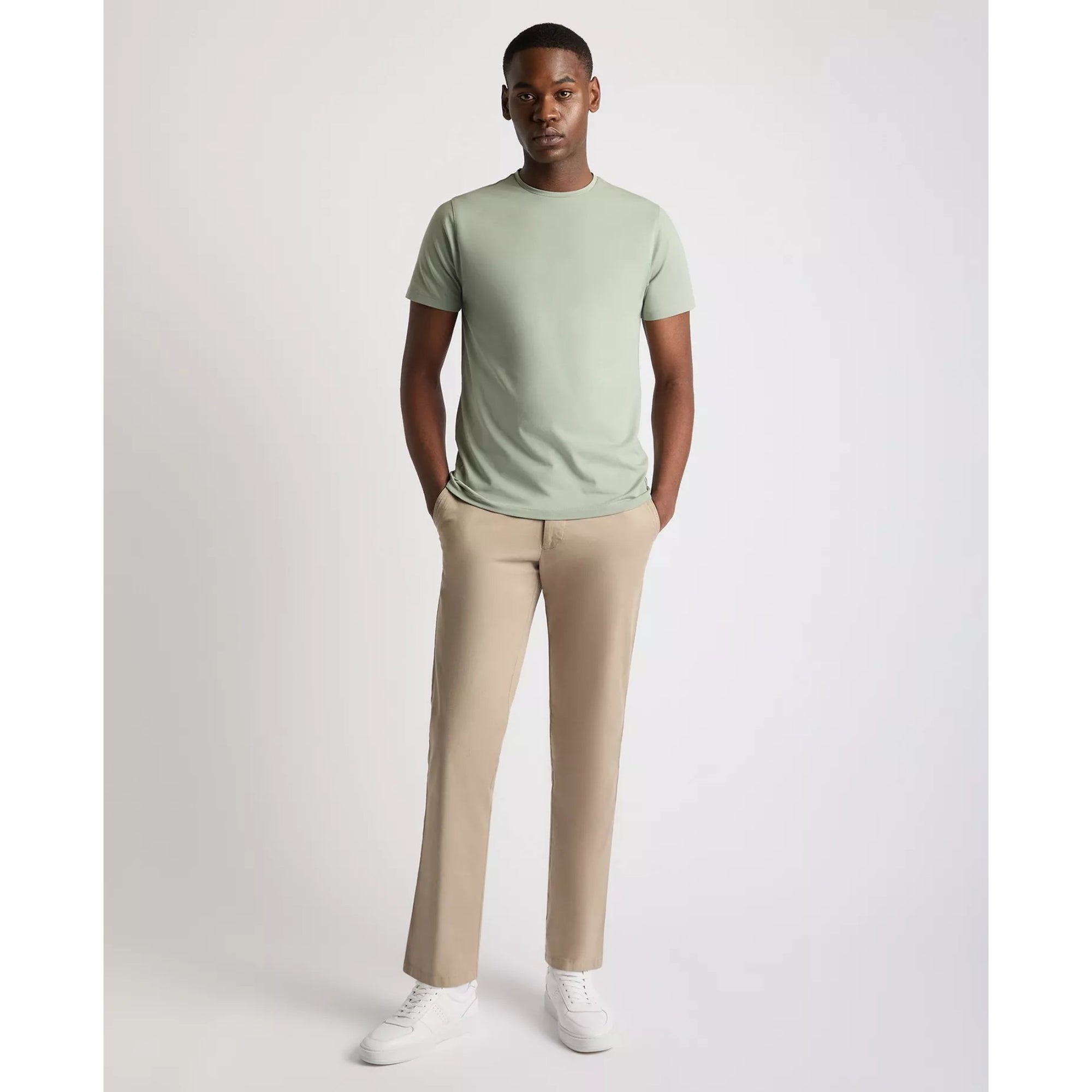 Man wearing a light green t-shirt and beige pants on a white background