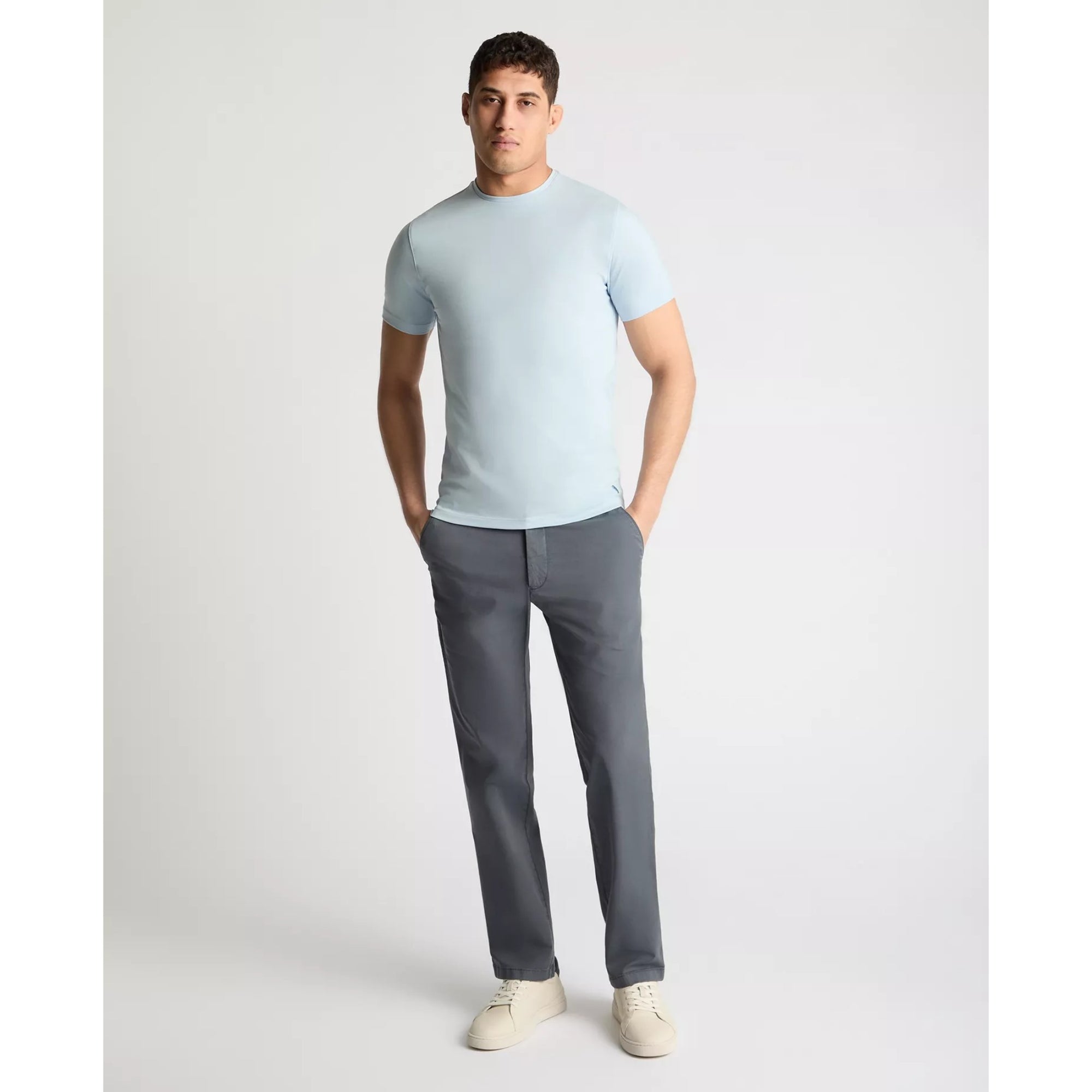 Man wearing a light blue t-shirt and gray pants on a white background