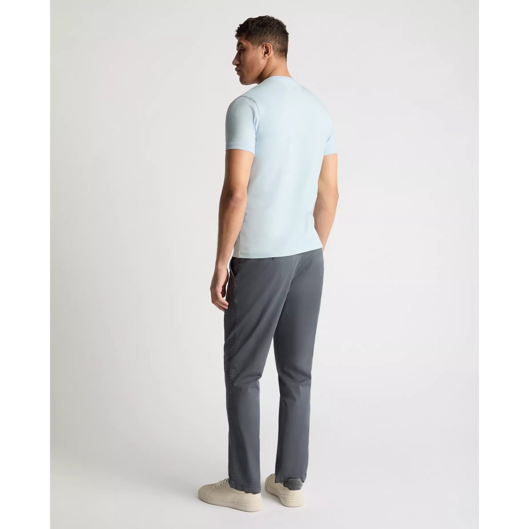 Man wearing a light blue t-shirt and gray pants on a white background