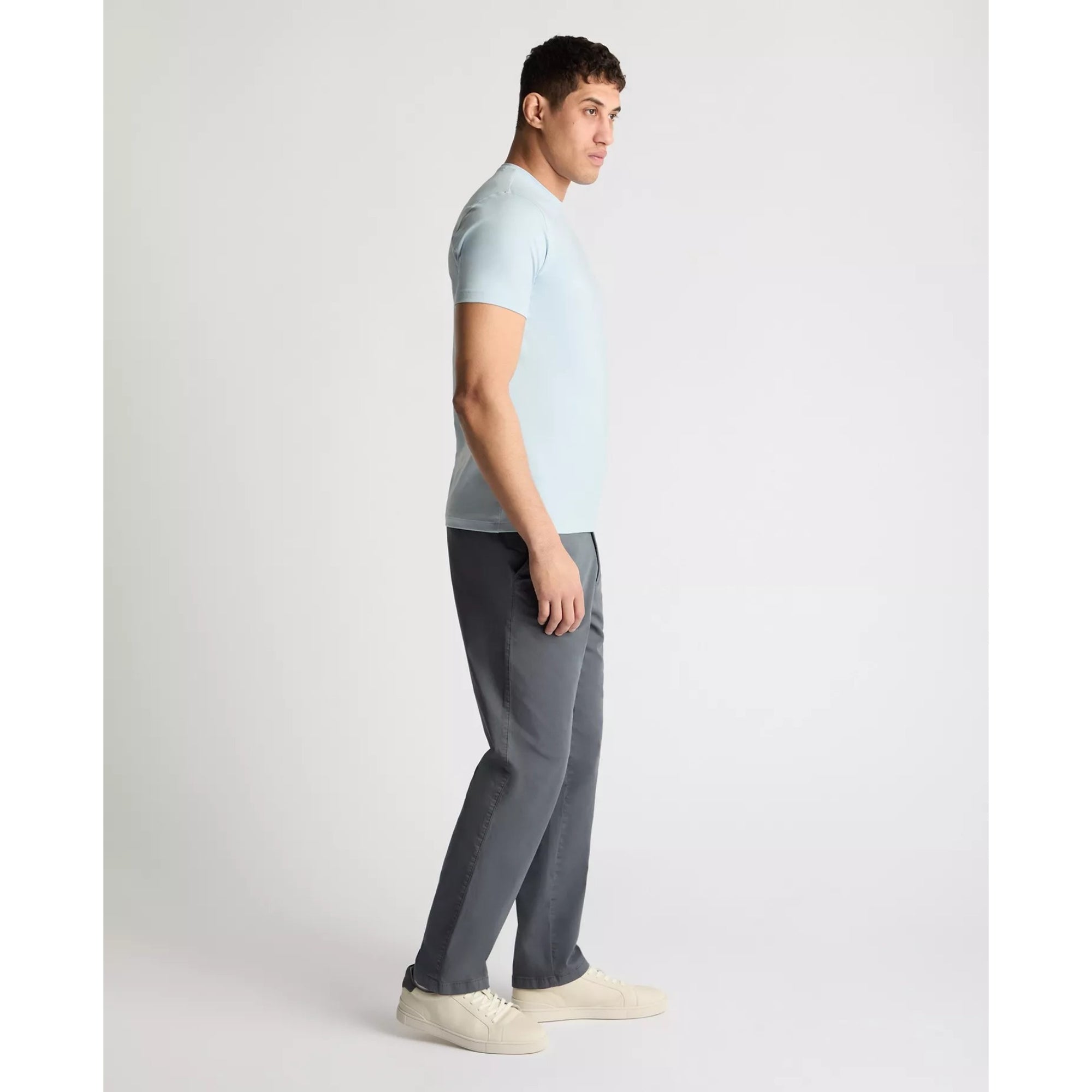 Man wearing a light blue t-shirt and gray pants on a white background