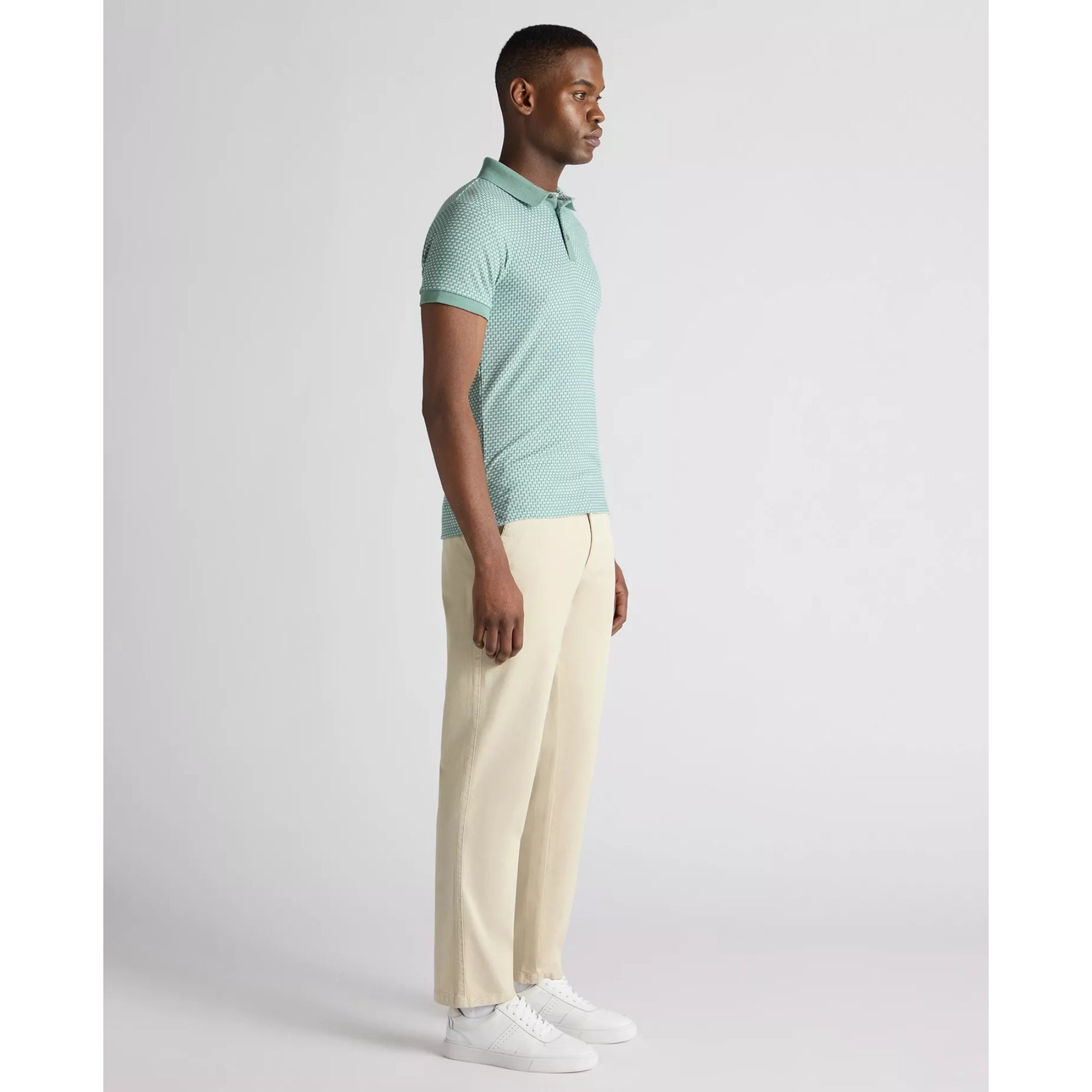 Man wearing a light green polo shirt and beige pants on a white background