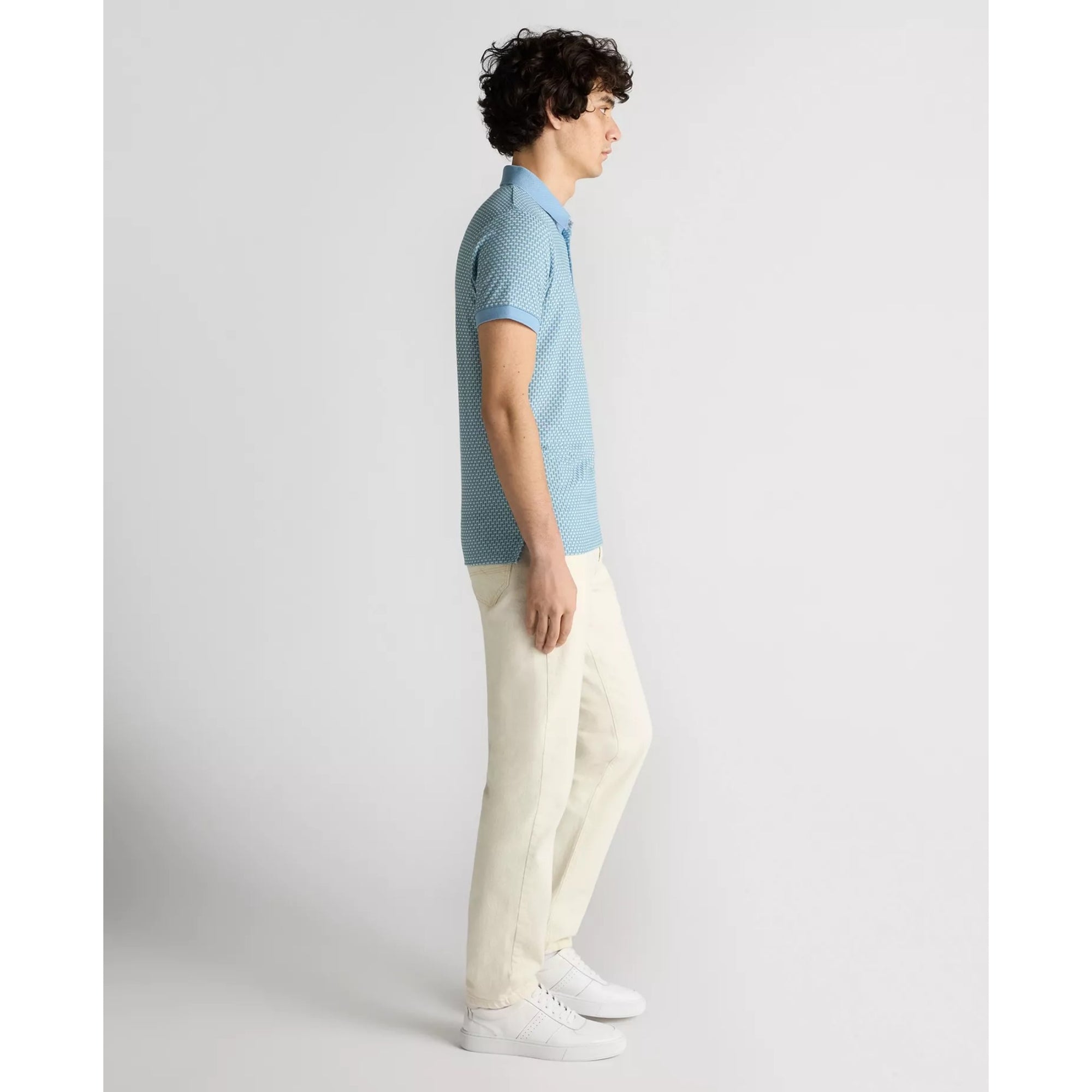 Man wearing a light blue patterned shirt and white pants on a plain background